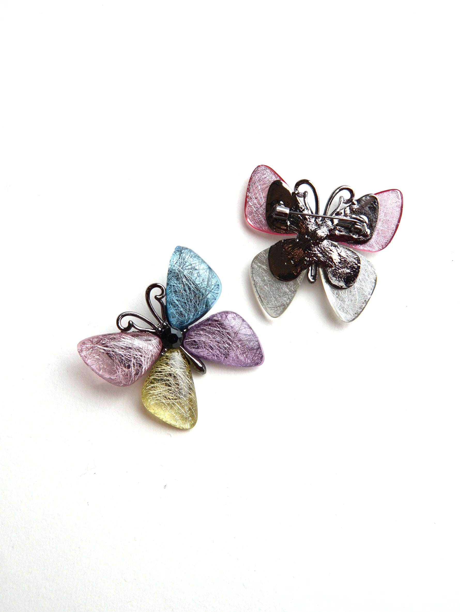 Mai multe broșe fluture colorate, așezate decorativ, fiecare cu variații subtile de culoare.