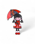 Broșă veselă cu o fetiță îmbrăcată în roșu, cu umbrelă roșie și neagră, un accesoriu plin de farmec.