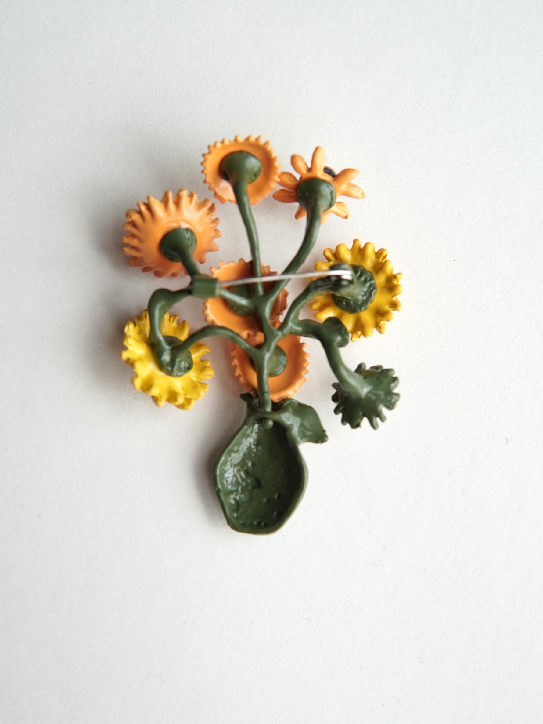 Detaliu de aproape al broșei cu vază și flori, evidențiind textura și cromatica florală.