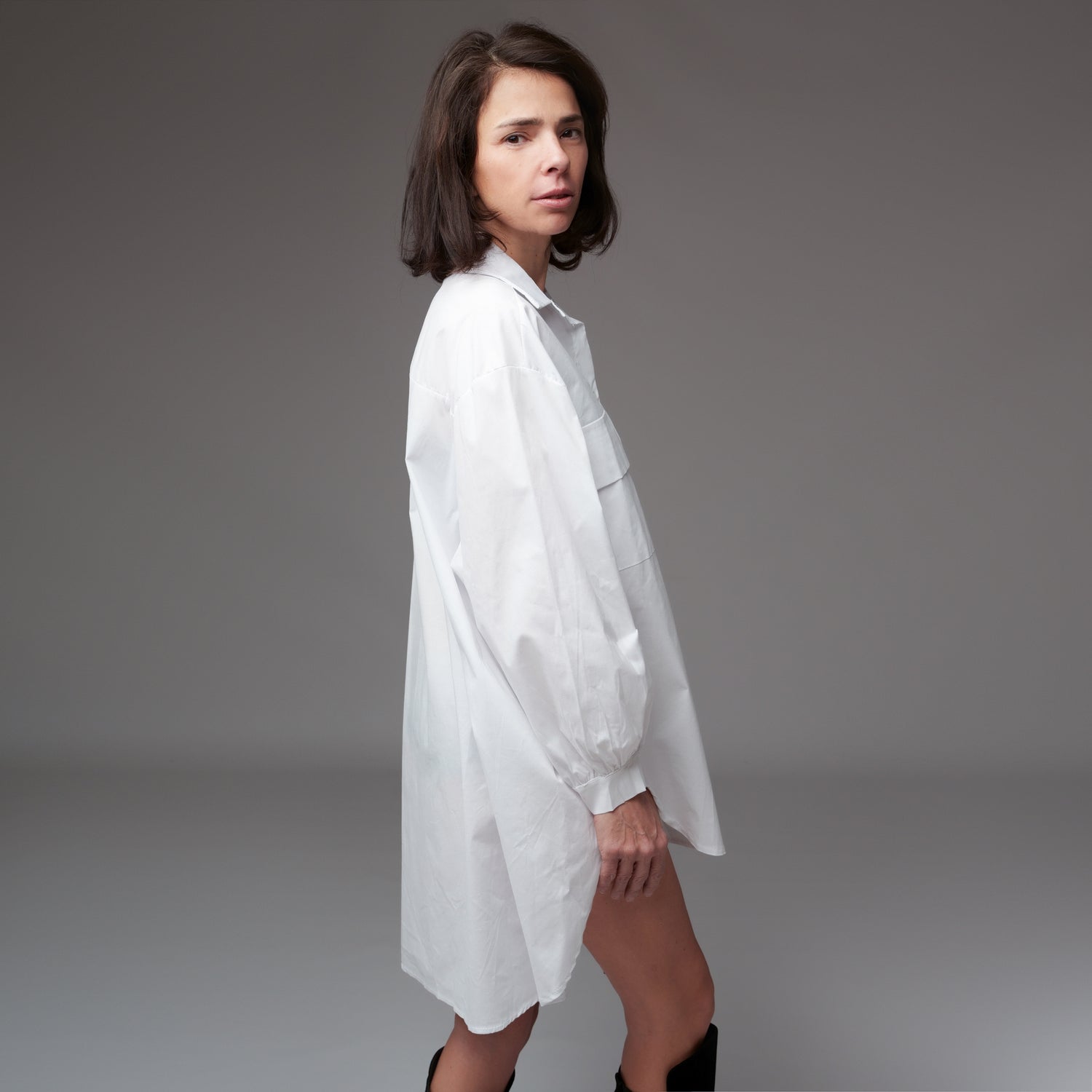 Cămașă albă lungă cu croială asimetrică, vedere din lateral, purtată de model cu păr brunet