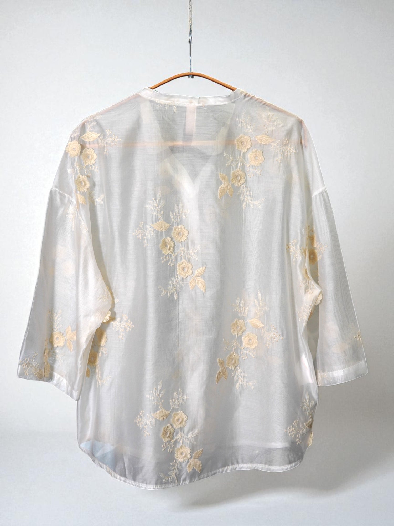 Spatele unei cămăși elegante crem, cu broderie florală bej și umeri căzuți