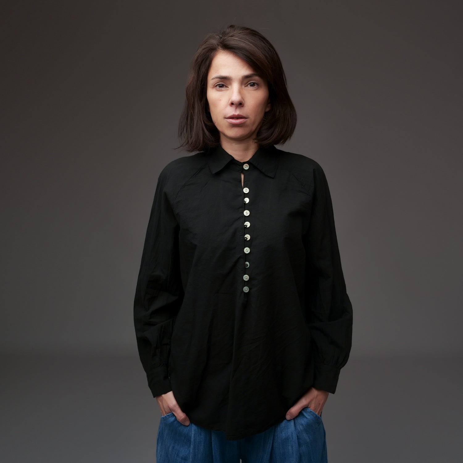 Cămașă din bumbac moale negru purtată de model, cu croială dreaptă și nasturi centrali.