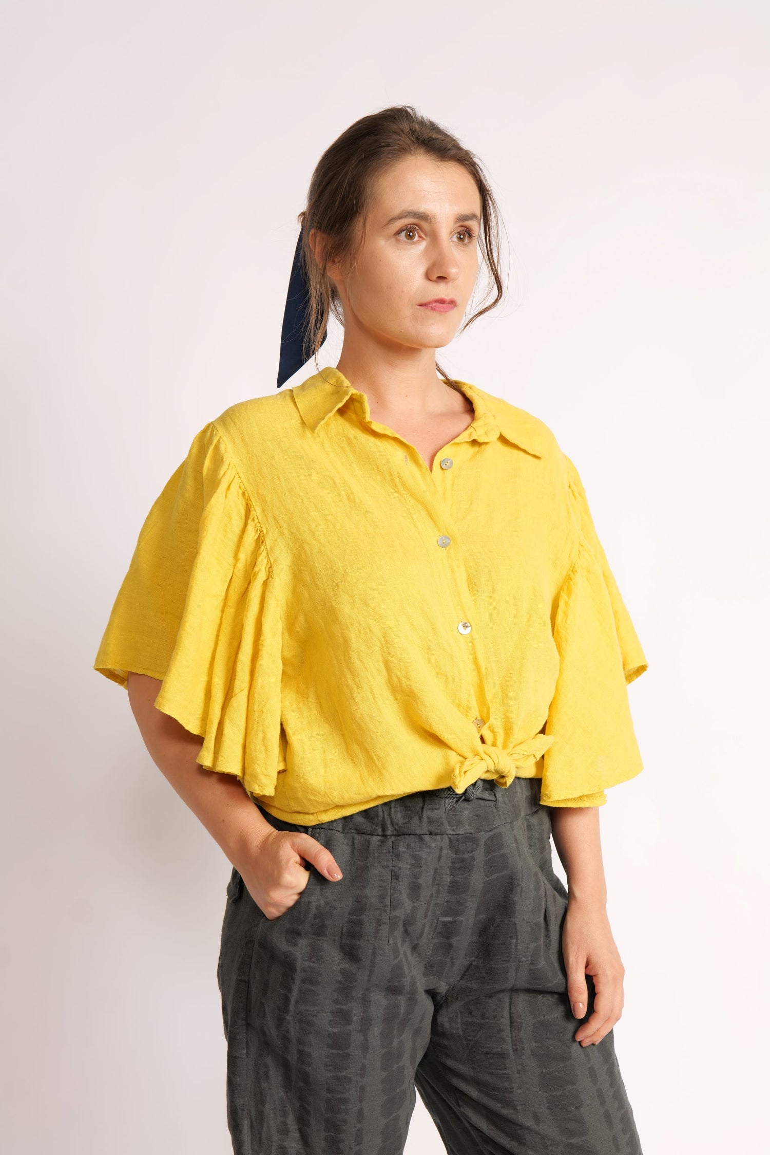  Cămașă galbenă din in purtată legată în față tip crop top, cu mâneci fluture și închidere cu nasturi.