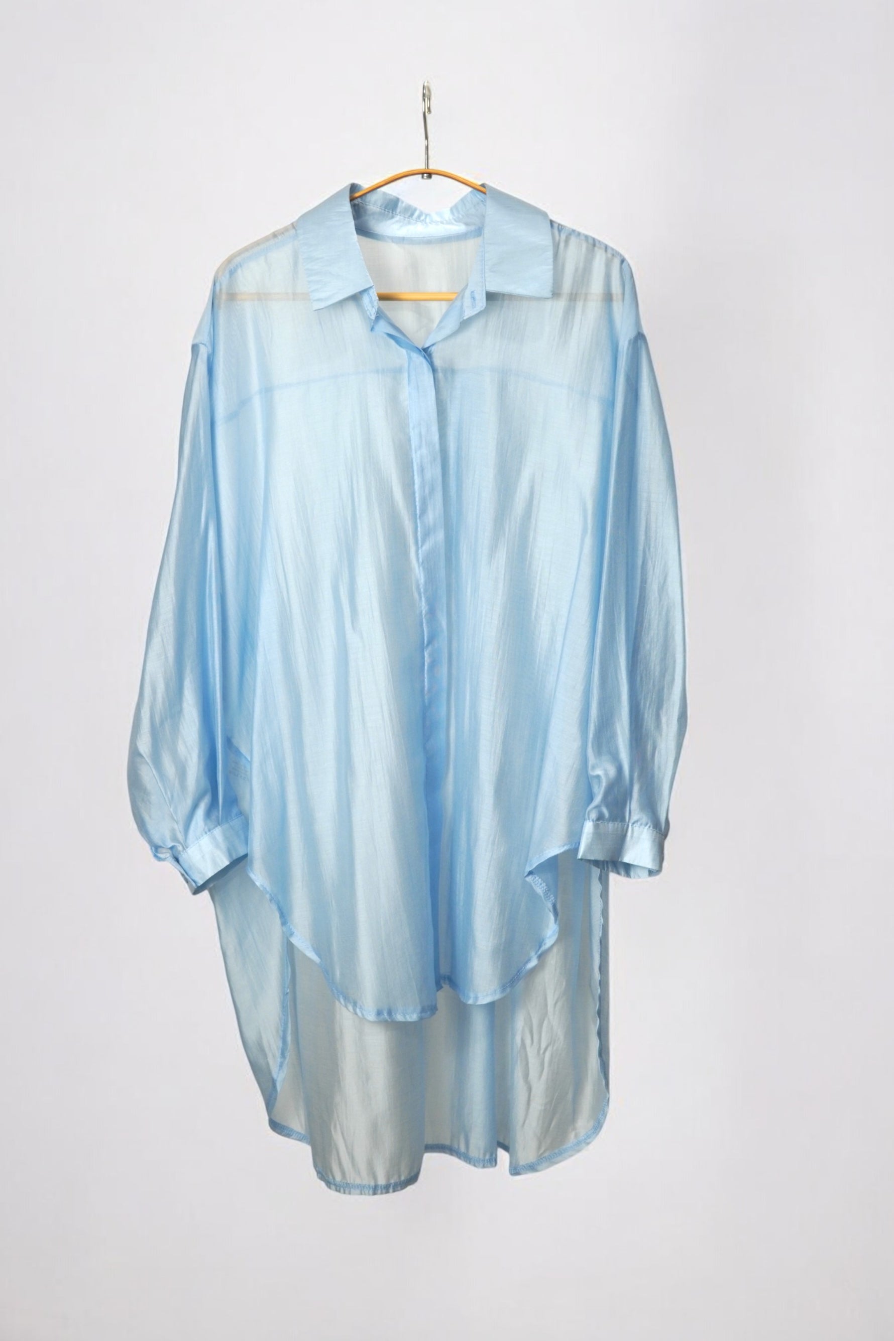 Cămașă oversized bleu pastel, din material ușor și transparent, afișată pe umeraș, fundal alb.