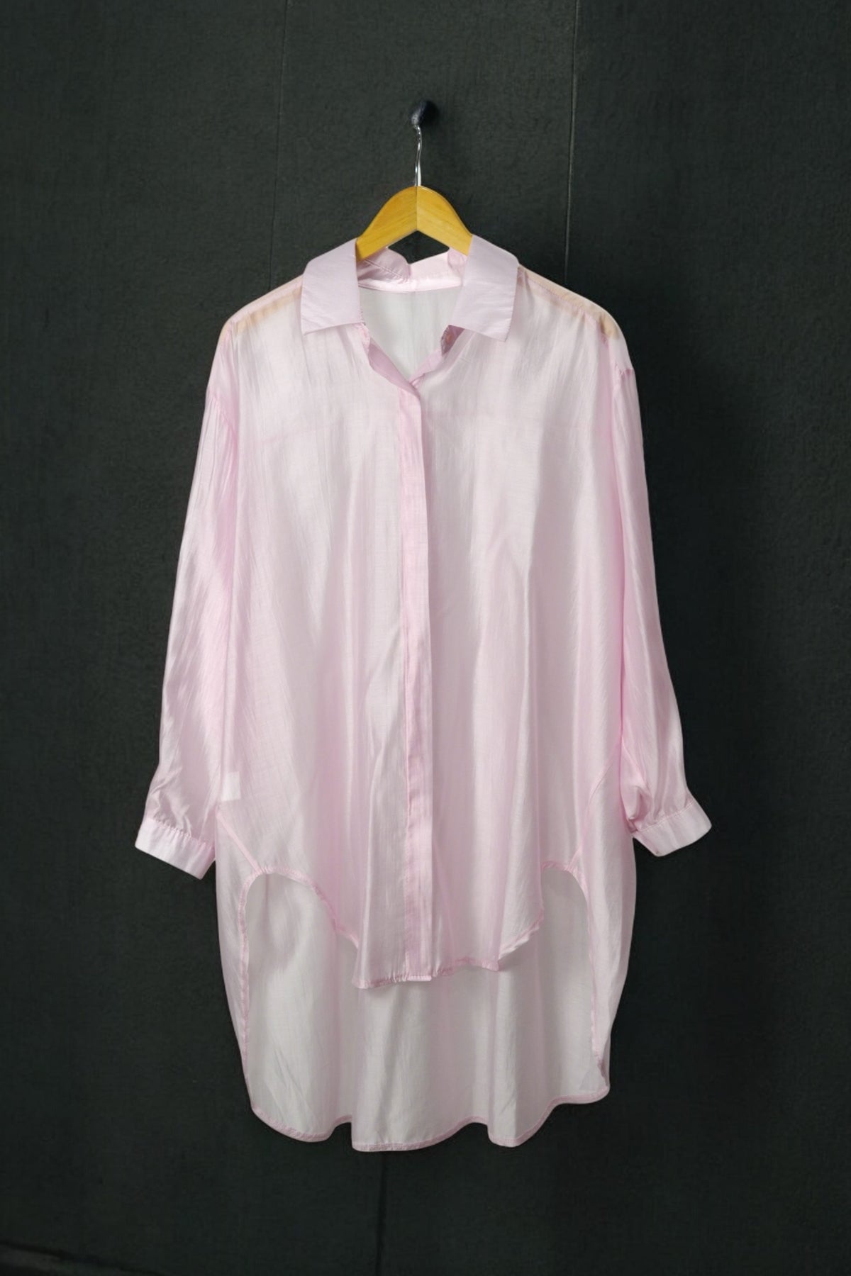 Cămașă oversized roz pastel, cu material ușor transparent, prezentată pe umeraș, fundal gri.