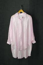 Cămașă oversized roz pastel, cu material ușor transparent, prezentată pe umeraș, fundal gri.