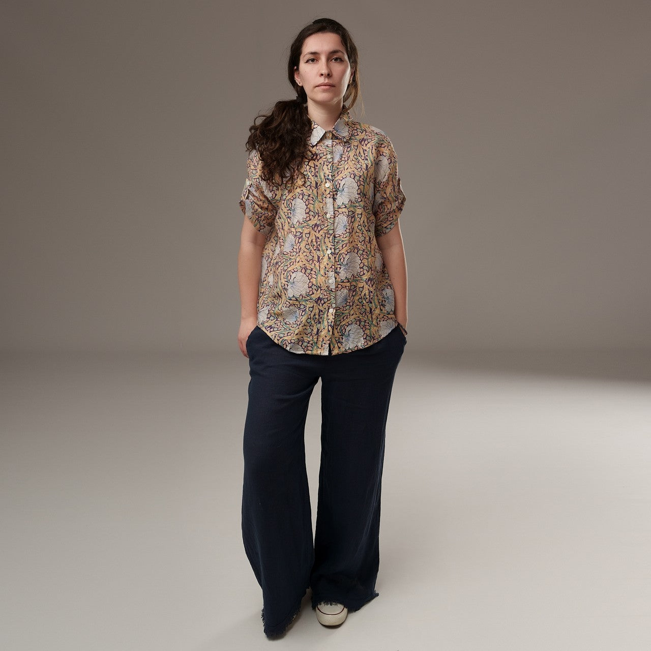  Cămașă din rayon cu imprimeu floral în nuanțe calde de bej, mânecă scurtă și croială lejeră, purtată cu pantaloni largi bleumarin.