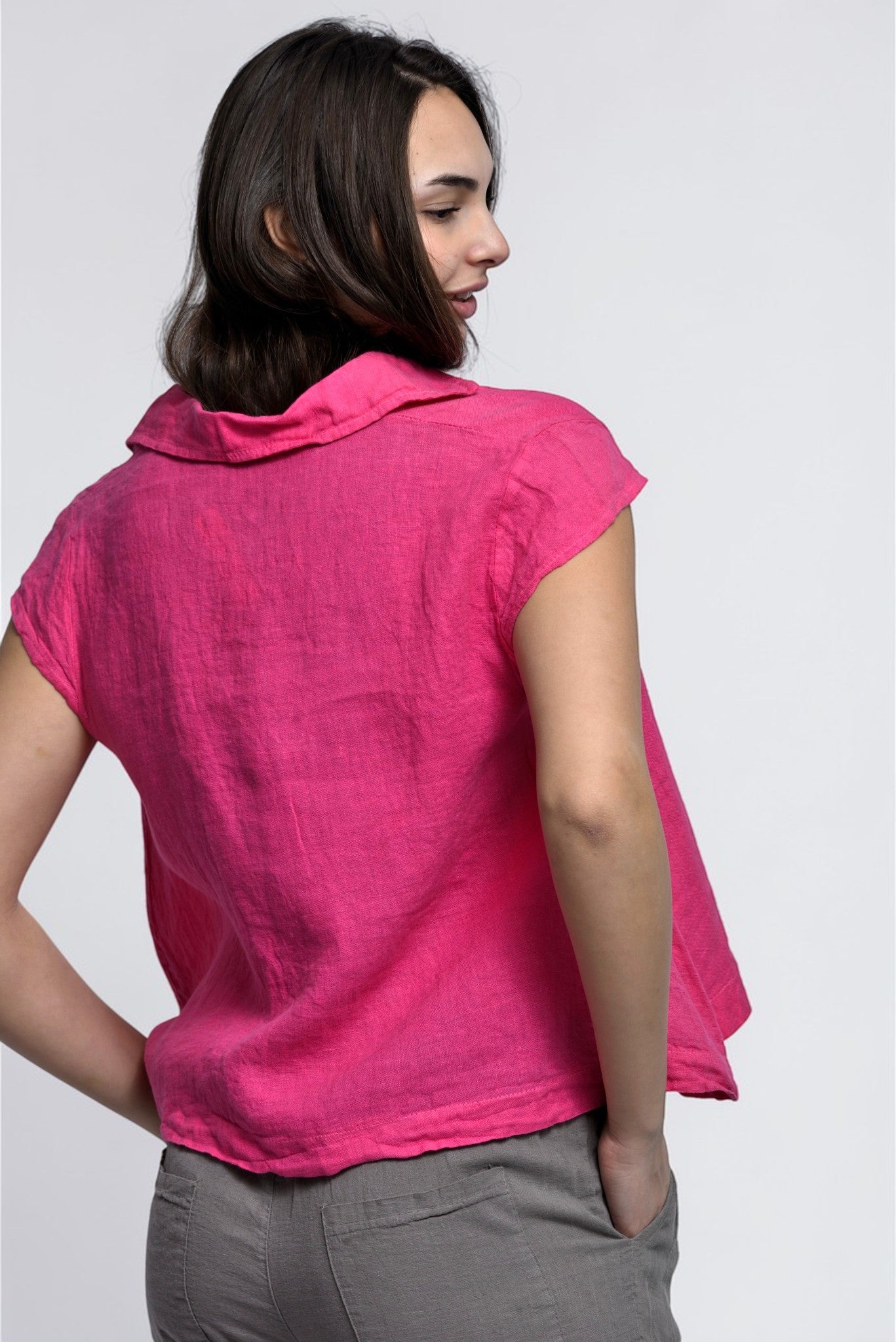 Spatele unei cămăși scurte din in roz cu croială amplă și cădere naturală, potrivită pentru ținute de vară.