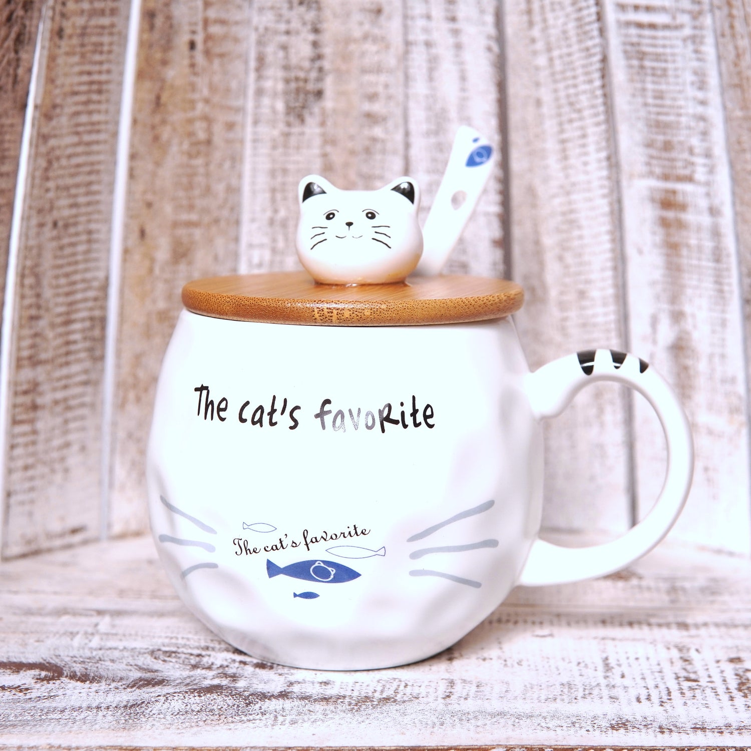 Cană albă din ceramică cu capac de lemn și linguriță, imprimeu „The Cat’s Favorite” cu desen de pește și mustăți.