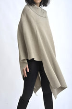 Vedere laterală a unei cape tricotate bej, cu linie asimetrică și volum generos