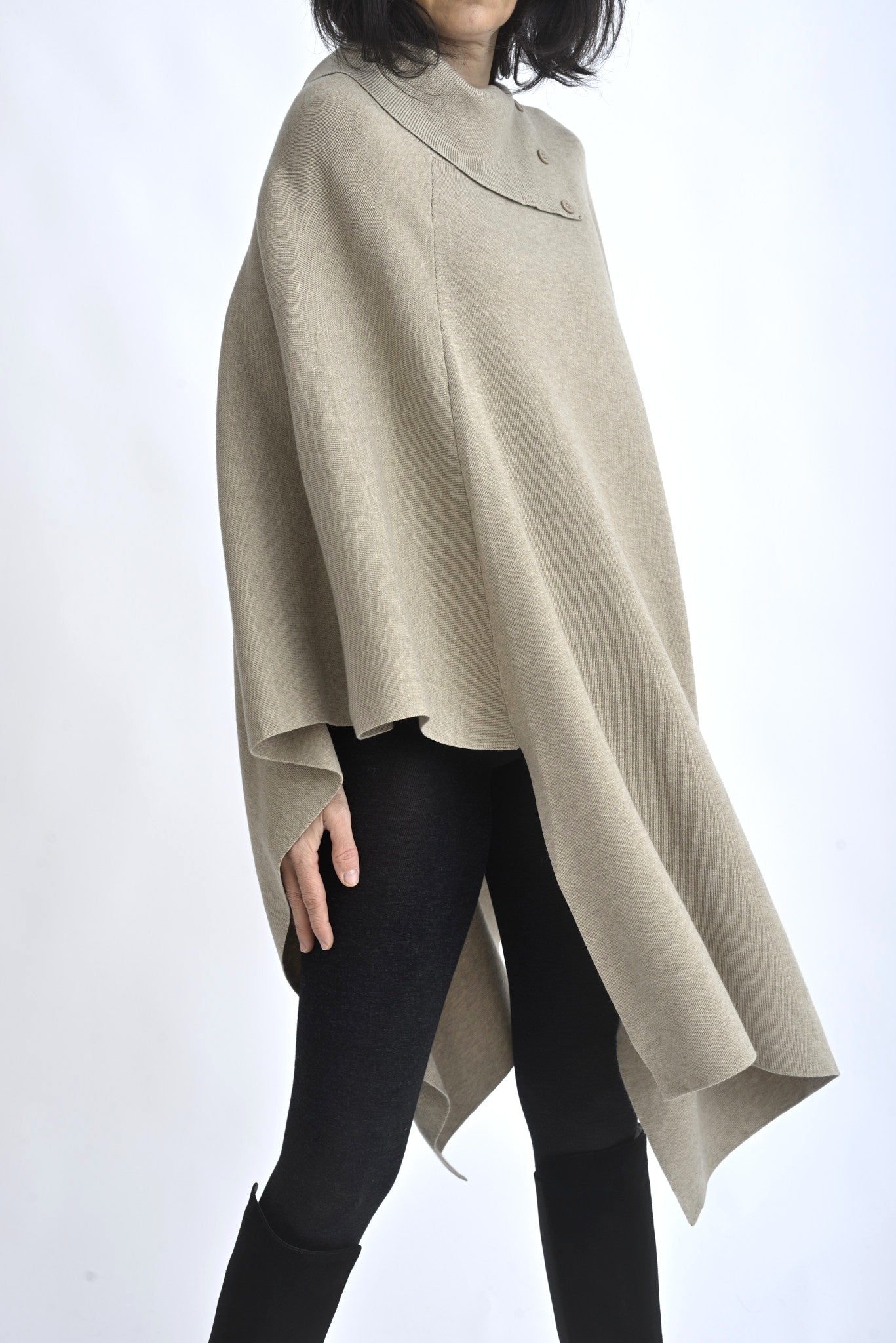 Vedere laterală a unei cape tricotate bej, cu linie asimetrică și volum generos