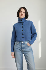 Detaliu de textură striată și nasturi negri pe cardigan scurt albastru cu guler înalt.