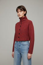 Cardigan scurt roșu, cu nasturi frontali și guler înalt, purtat într-o ținută casual cu jeanși.