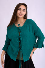 Model poartă cardigan tricotat fucsia, scurt, cu șnur frontal și umeri căzuți, prezentare din față pe fundal alb.