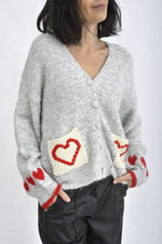 Buzunare frontale tricotate ale cardiganului gri, decorate cu aplicații în formă de inimă