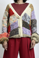 Cardigan tricotat multicolor cu umeri căzuți, închidere cu nasturi și textură groasă, purtat peste top bordo.