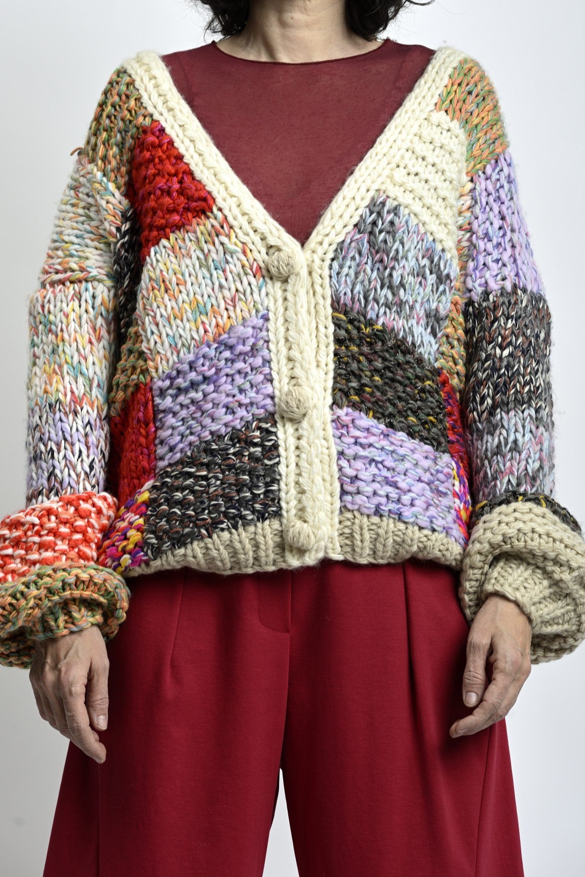 Cardigan tricotat multicolor cu umeri căzuți, închidere cu nasturi și textură groasă, purtat peste top bordo.