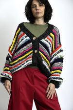 Cardigan tricotat multicolor cu bază neagră, umeri căzuți și nasturi din lemn, purtat peste top verde.