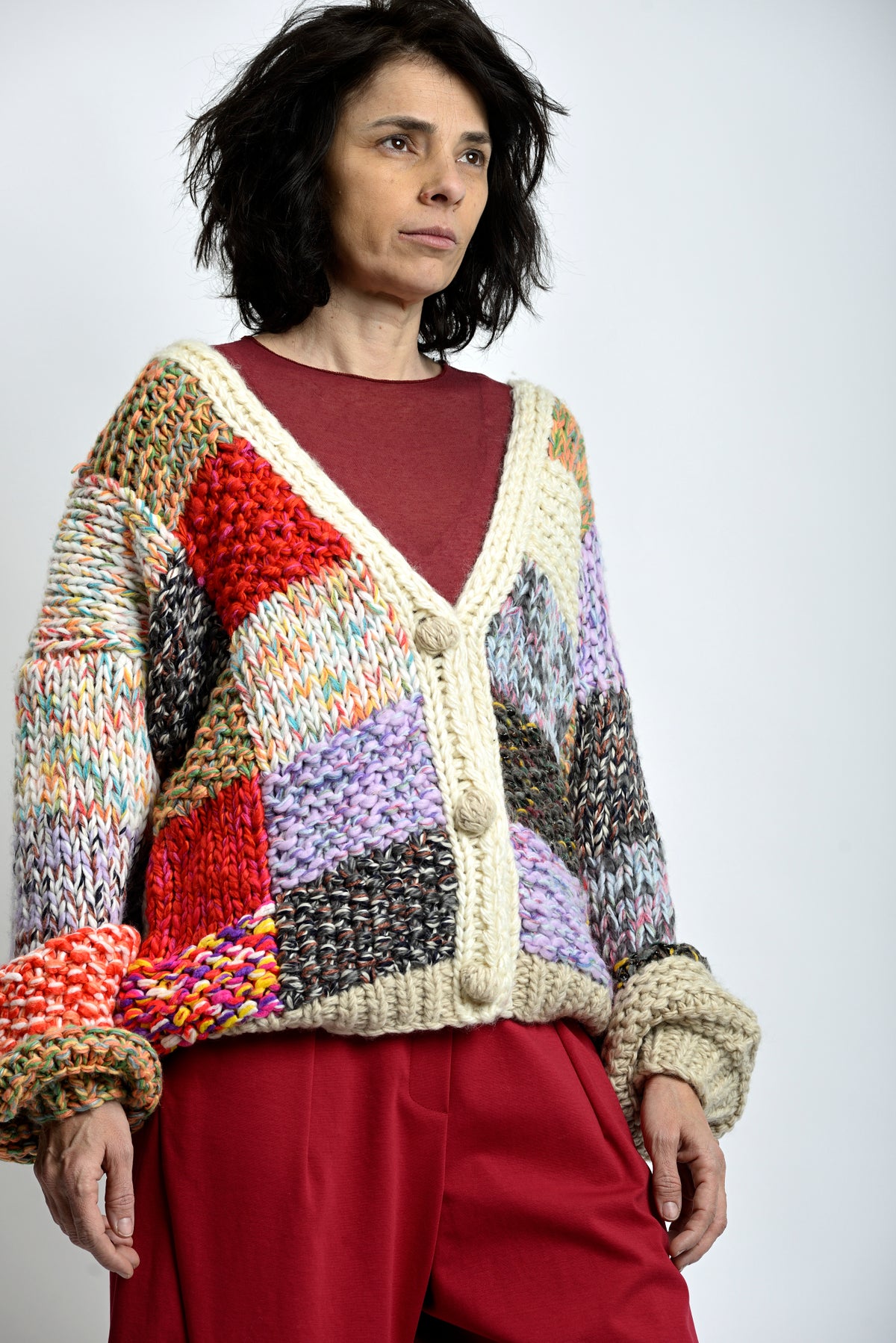 Cardigan tricotat multicolor văzut din profil, cu umeri căzuți și mâneci lungi cu manșete rulate.