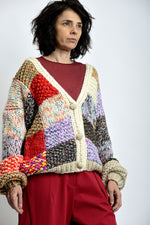 Cardigan tricotat multicolor văzut din profil, cu umeri căzuți și mâneci lungi cu manșete rulate.