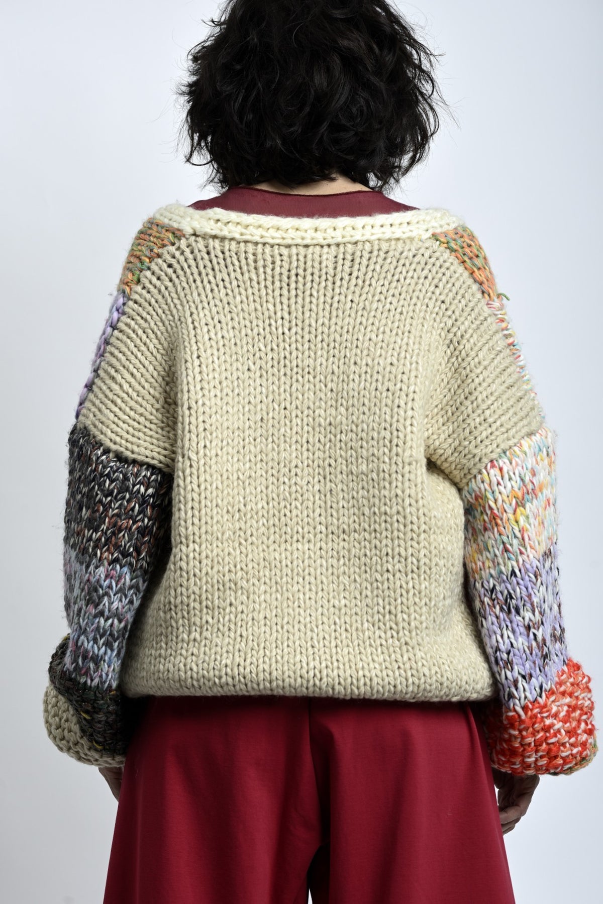 Spatele cardiganului tricotat din fir gros, culoare crem, croială relaxată și lungime medie.