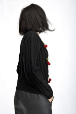 Detaliu aplicații cireșe din material textil, pe cardigan tricotat negru.