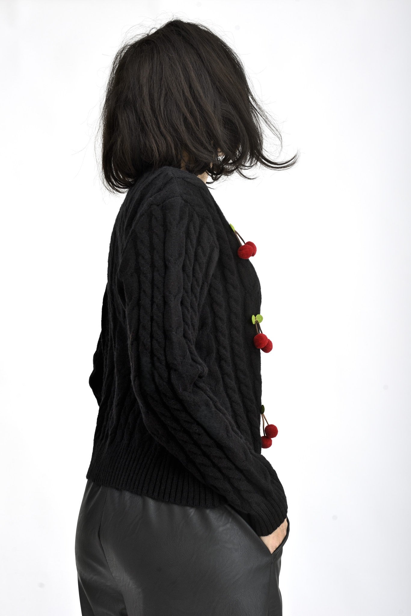 Detaliu aplicații cireșe din material textil, pe cardigan tricotat negru.