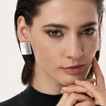 Cercei pătrați din aluminiu reciclat, cu design geometric și linii curate, purtați de o femeie pentru un look contemporan.