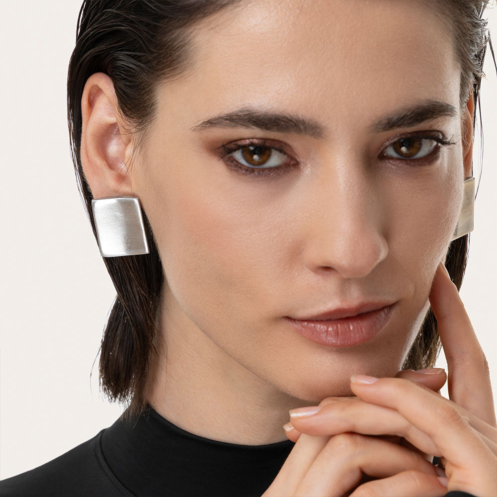 Cercei pătrați din aluminiu reciclat, cu design geometric și linii curate, purtați de o femeie pentru un look contemporan.