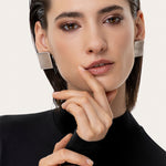 Cercei statement cu formă pătrată, aspect modern și finisaj satinat, prezentați pe model.