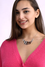 Colier argintiu format din multiple tije subțiri metalice, purtat pe model îmbrăcată într-un pulover roz tricotat, vedere din trei sferturi.