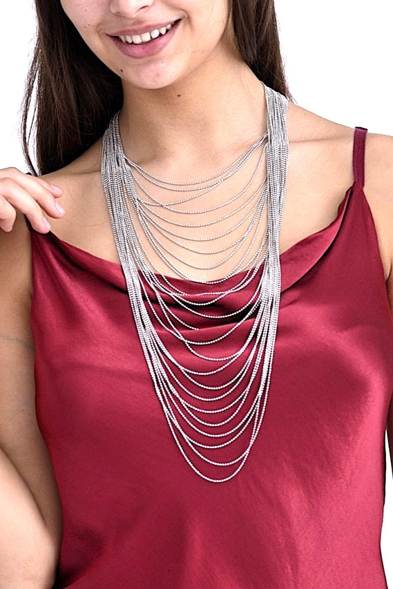 Colier multistrat cu lanțuri fine și mărgele metalice lucioase, purtat pe o bluză roșie din satin.