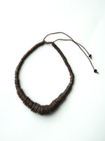 Colier din lemn văzut lateral, arătând flexibilitatea șnurului și forma discurilor.