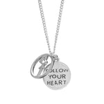 Gros-plan cu pandantivul gravat „Follow Your Heart” și simbol abstract, pe lanț placat cu argint