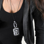 Colier cu pandantiv geometric format din trei dreptunghiuri din aluminiu reciclat, purtat pe șnur negru reglabil.