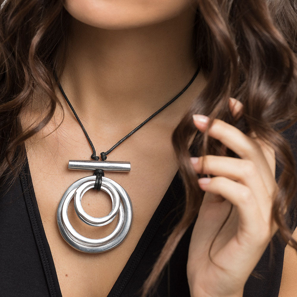 Colier cu pandantiv format din cercuri concentrice din aluminiu reciclat, purtat la gât pe șnur negru reglabil.