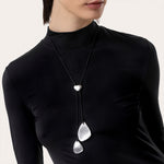 Colier cu pandantiv în formă de petale stilizate din aluminiu reciclat, purtat pe șnur negru reglabil, cu design modern și delicat.