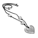 Colier lung cu șnur negru și pandantiv în formă de inimă din aluminiu reciclat, accesorizat cu trei mici inimi, purtat pe un outfit negru.