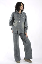 Vedere integrală a compleului din denim gri, cu bluză cu nasturi și pantaloni lungi, purtat lejer.