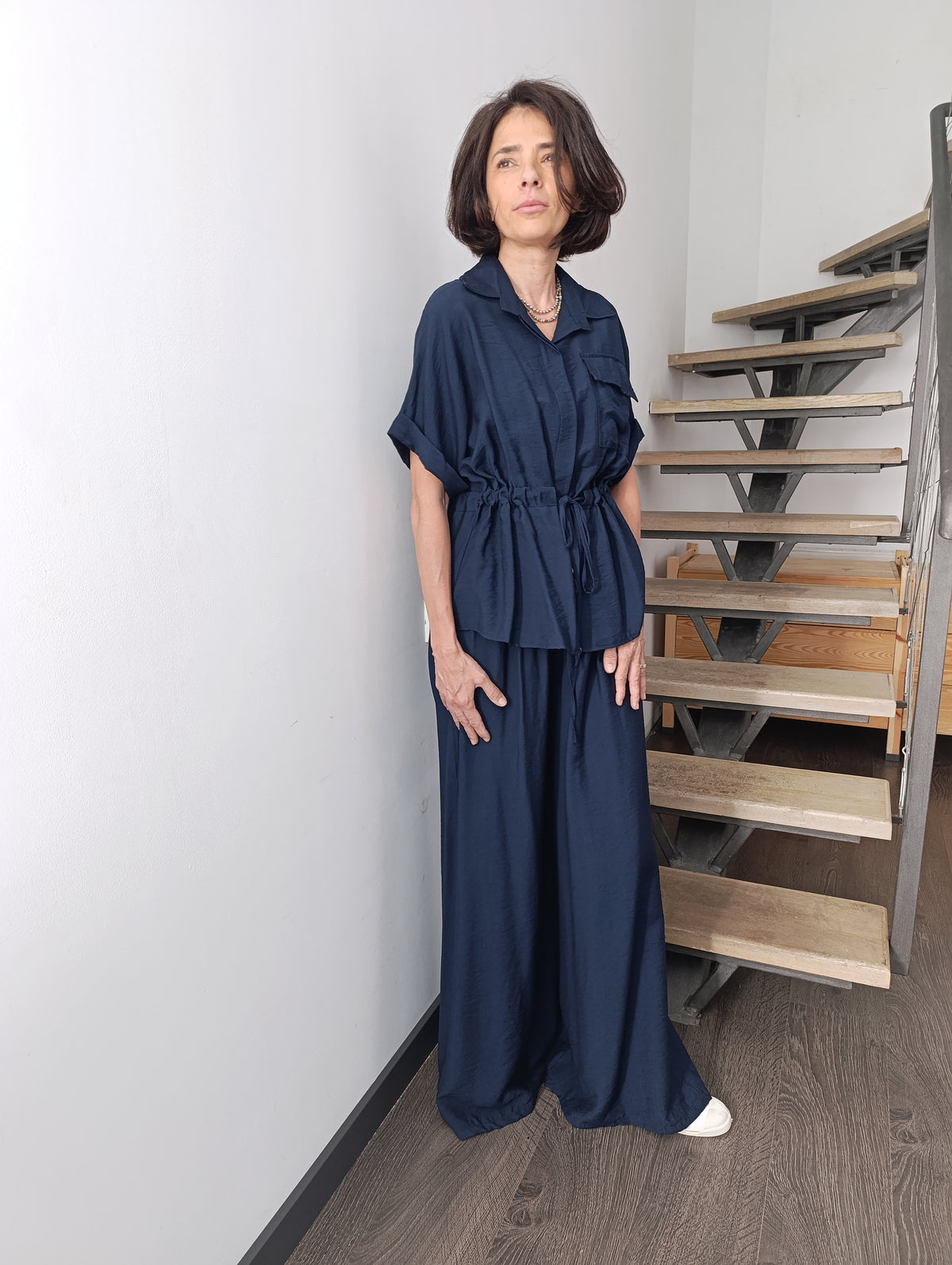 Compleu satinat bleumarin cu bluză cu cordon în talie și pantaloni largi, purtat de model în fața unei scări interioare