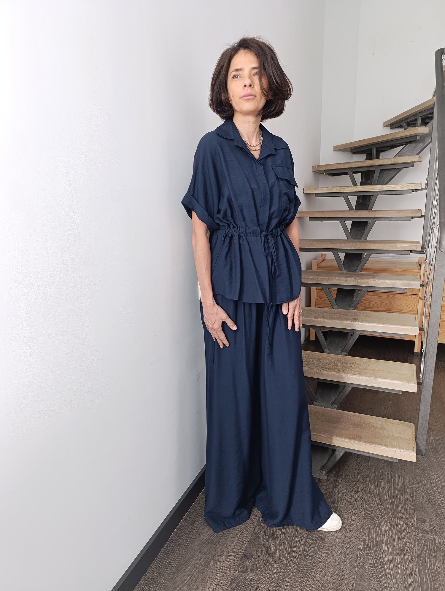Compleu satinat bleumarin cu bluză cu cordon în talie și pantaloni largi, purtat de model în fața unei scări interioare