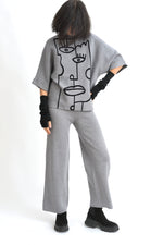 Vedere laterală a compleului cu top imprimat cu portret stilizat și pantaloni drepți, croială relaxată.