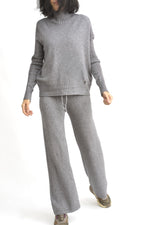 Vedere dinamica a compleului gri din tricot, format din top căzut pe umeri și pantaloni largi.