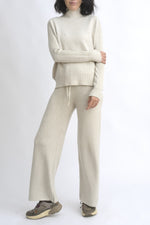 Compleu din tricot bej format din top cu dungi rib și umeri căzuți, asortat cu pantaloni largi din același material.