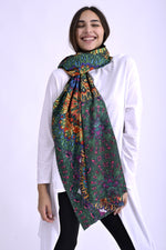 Model purtând o eșarfă colorată cu imprimeu etnic în nuanțe vii de verde, roz, portocaliu și albastru, accesorizând o ținută casual cu bluză albă.