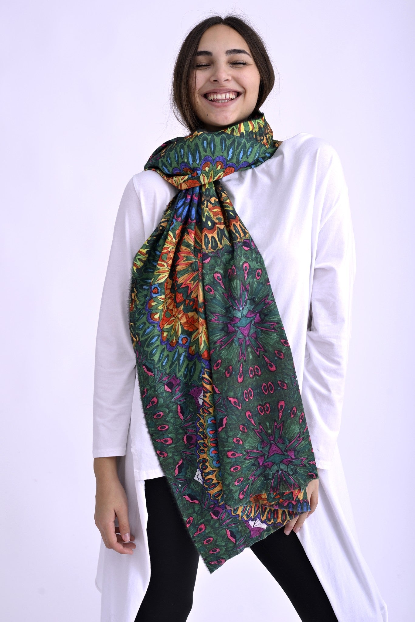 Model purtând o eșarfă colorată cu imprimeu etnic în nuanțe vii de verde, roz, portocaliu și albastru, accesorizând o ținută casual cu bluză albă.