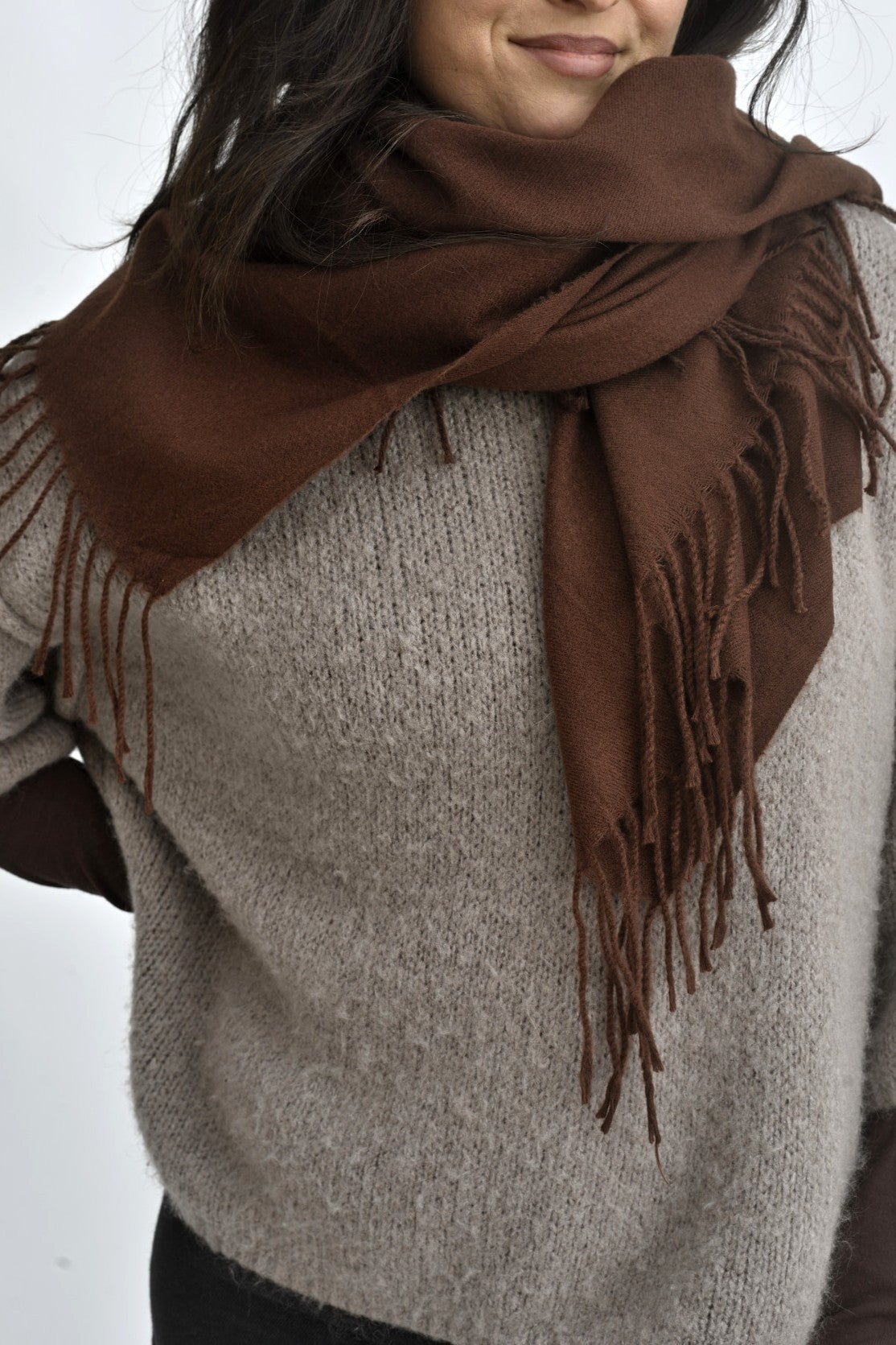 Eșarfă maro, cu franjuri discrete, așezată în jurul gâtului peste un pulover bej, într-o stilizare calmă și versatilă.