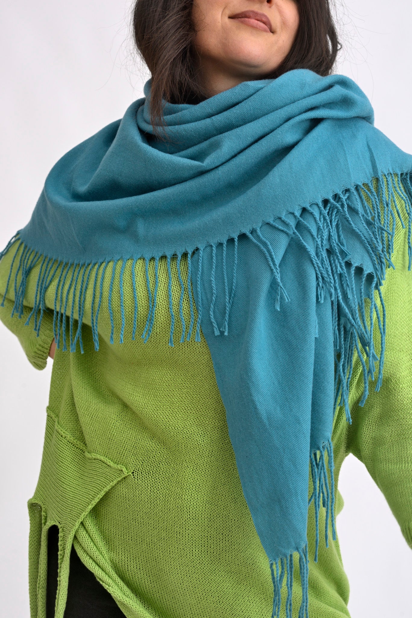 Eșarfă turcoaz cu franjuri fine, purtată lejer peste un pulover verde, evidențiind textura moale și drapajul natural.