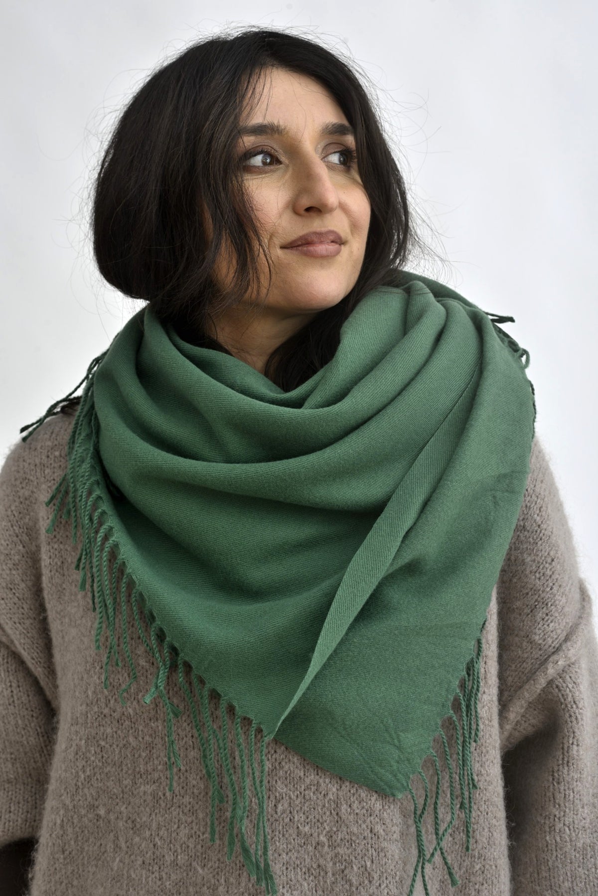 Eșarfă verde cald, cu franjuri delicate, purtată clasic peste un pulover neutru, într-o compoziție echilibrată și atemporală.
