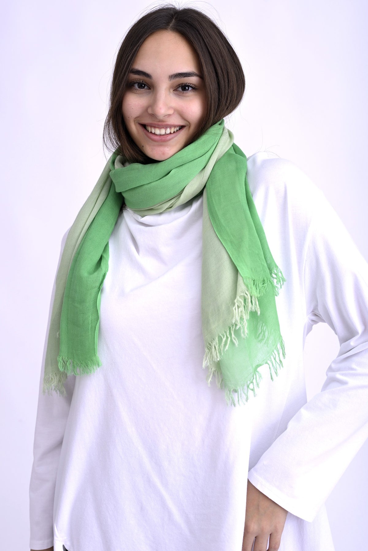 Model purtând o eșarfă în degrade de verde, cu franjuri fine la capete, accesorizând o ținută casual cu bluză albă.